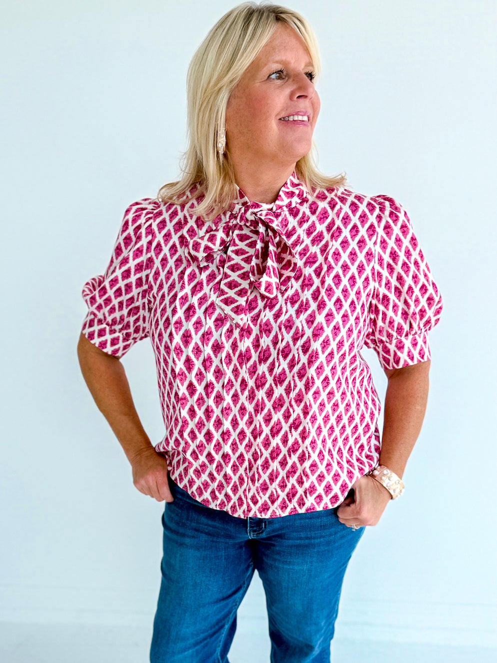 Woman wearing a pink patterned blouse with a bow tie against a light blue background